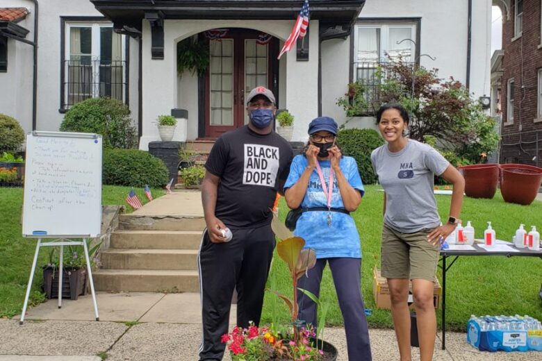 Three people smiling in front of house.