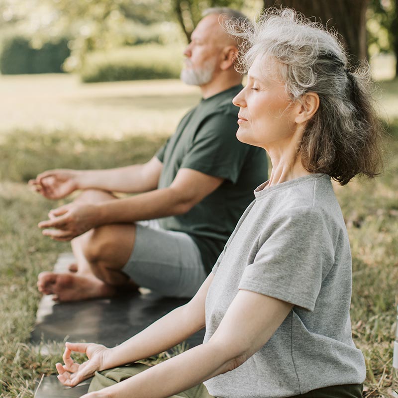 Two people sitting in the grass doing yoga.